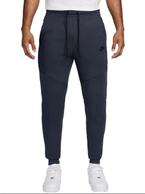 Mörkblå Nike mjukisbyxor - Säljer ett par mörkblå mjukisbyxor från Nike med smal passform och ribbade muddar vid bensluten. Byxorna har dragsko i midjan och sidofickor. Tillverkade i mjukt bomullsmaterial och har en diskret Nike-logga på låret.