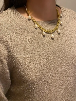 Guldfärgat halsband med pärldroppar - Snyggt halsband i guldfärgad rostfritt med droppformade vita pärlor som hänger längs kedjan. Kedjan är grov och ger ett trendigt intryck, medan pärlorna tillför en elegant touch. Perfekt accessoar för att lyfta din outfit.