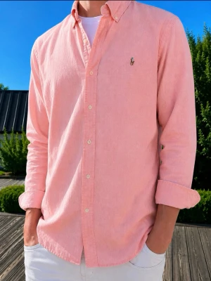 Ljusrosa skjorta från Ralph Lauren - LAX ROSA FÖRG(MODDELEN ÄR 185CM OCH VÄGER 75 KG)Klassisk ljusrosa skjorta från Ralph Lauren med button-down krage och broderad logga på bröstet. Skjortan har långa ärmar och vita knappar framtill. Tillverkad i mjuk bomull och har en avslappnad passform.
