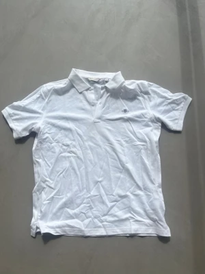 Vit pikétröja från Gant - Klassisk vit pikétröja från Gant med korta ärmar och liten logga broderad på bröstet. Tröjan har krage och knappar framtill, perfekt för en clean och stilren look. Tillverkad i mjuk bomull som känns skön mot huden.