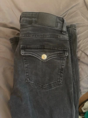 Svarta skinny jeans med fickdetalj - Säljer ett par svarta bootcut jeans med en snygg fickdetalj med silverknapp. Jeansen har låg midja och är perfekta till en trendig streetstyle-look. Materialet är stretchigt denim för extra komfort. Modell 90s boot i short length från lager 157.