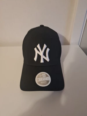 Svart New Era Yankees keps - Snygg svart keps från New Era med klassisk New York Yankees-logga broderad i vitt framtill. Modellen är 9FORTY och har justerbar rem bak för perfekt passform. Tillverkad i slitstarkt material och passar perfekt till streetwear-stilen. Kepsen har ingen laå men den är aldrig använd 