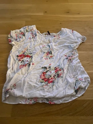 Vit blommig topp från ONLY - Söt vit topp från ONLY med blommigt mönster i rosa och rött. Toppen har korta ärmar och rund halsringning. Perfekt för en fräsch och somrig look. Tillverkad i mjuk bomull som känns skön mot huden.