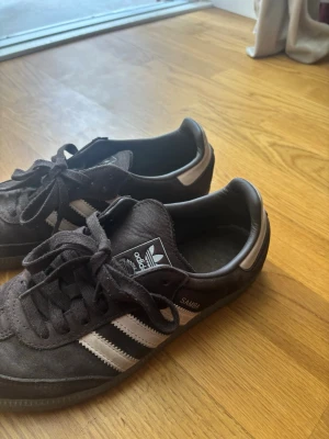 Adidas Samba - Klassiska Adidas Samba sneakers i brun mocka med ljus rosa detaljer och de ikoniska tre ränderna på sidan. Låg modell med snörning och gummisula. Knappast använda, säljer då modellen är för platt för mina fötter💕