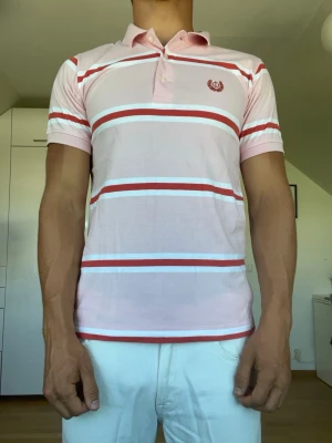 Randig rosa piké  - Randig piké från Oscar Jacobson tillverkad i 100% bomull. Strl S. Inga defekter. Modellen är 178 cm och väger 77 kg. Hör gärna av dig vid frågor!