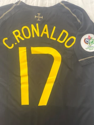 Portugal C. Ronaldo Nike tröja svart - Säljer en svart Portugal fotbollströja från Nike med C. Ronaldo och nummer 17 i gult. Tröjan har officiellt landslagsmärke, gul Nike-logga och patch från VM 2006 på ärmen. Tillverkad i lätt och ventilerande material, perfekt för träning eller match.