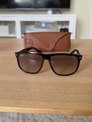 Svarta Ray-Ban Boyfriend solglasögon - Klassiska svarta Ray-Ban Boyfriend solglasögon med bred båge och mörka tonade glas. Säljs med original brunt Ray-Ban-fodral. Perfekt accessoar för soliga dagar och ikonisk stil.