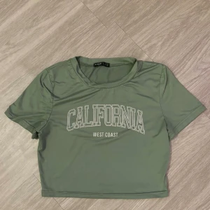 Grön croppad topp med tryck - Trendig ljusgrön croppad topp från Shein med texten 'California West Coast' tryckt framtill. T-shirten har korta ärmar och rund halsringning, perfekt för en avslappnad stil.