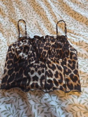 Leopardmönstrat linne från SHEIN - Snygg leopardmönstrat linne från SHEIN i storlek XS. Toppen har smala axelband och croppad passform, perfekt för att sticka ut. Tillverkad i ett mjukt syntetmaterial som känns bekvämt mot huden. Matcha med jeans eller kjol för en trendig look.
