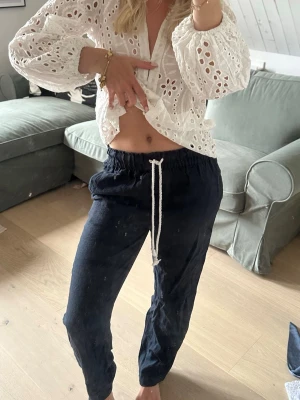 Marinblå linnebyxor  - Snygga mörkblå linnebyxor med avslappnad passform och vit dragsko i midjan. Byxorna har raka ben och resår i midjan för extra komfort. Perfekta för en stilren look.