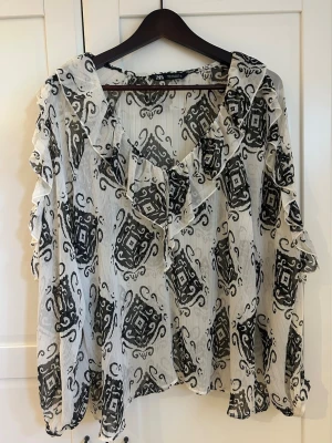Mönstrad volangblus från Zara - Säljer en supersnygg oversized lite genomskinlig blus från Zara med svartvitt mönster och volangdetaljer längs ringningen. Blusen är helt oanvänd och i nyskick! Är i storlek L men passar även M! 💕💕