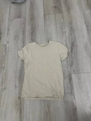 Beige t-shirt från lager 157 och svart Tommy Hilfiger t-shirt - Säljer två t-shirts: en enkel beige t-shirt från H&M i mjuk bomull med rund hals och korta ärmar, samt en svart t-shirt från Tommy Hilfiger med logga framtill. Båda har klassisk passform och passar perfekt till jeans eller shorts.