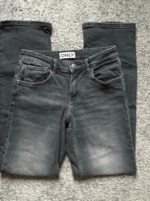 Svarta jeans från ONLY med tvättad look - Säljer ett par svarta jeans från ONLY med snygg tvättad effekt och klassisk femficksmodell. Jeansen har raka ben och normal midja. Materialet är mjukt denim som sitter skönt hela dagen. Perfekta för dig som gillar en avslappnad men trendig stil. 27/32