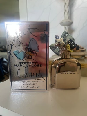 Marc Jacobs Perfect Charm EdP 50ml - Marc Jacobs Perfect Charm Eau de Parfum Collector Edition i 50 ml. Flaskan är metallic-roséguld med en unik kork dekorerad med färgglada charms och stjärnor. Förpackningen har en spegelblank finish och lekfull design. En ikonisk och samlarvänlig parfym. Endast testad!
