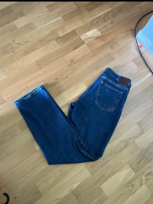Blå raka jeans från Lee - Säljer ett par klassiska blå jeans från Lee med rak passform och hög midja. Jeansen har fem fickor, gylf med dragkedja och knapp samt Lee-lapp bak i midjan. Tillverkade i slitstark denim, perfekta till vardagslooken.