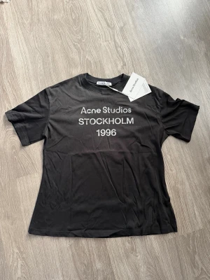 Svart Acne Studios t-shirt - Svart t-shirt från Acne Studios med tryck 'STOCKHOLM 1996' på bröstet. Klassisk passform med rund hals och korta ärmar. Perfekt för en clean och stilren look. Materialet är mjuk bomull som känns skönt mot huden.