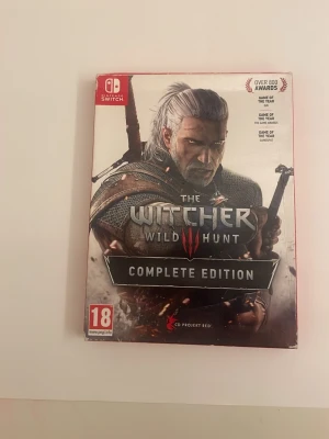 The Witcher 3 Wild Hunt Complete Edition - The Witcher 3: Wild Hunt Complete Edition till Nintendo Switch. Spelet har ett omslag med Geralt i fokus och innehåller en svart fodral med CD Projekt Red-loggan. Omslaget är mestadels grått, svart och rött. Perfekt för dig som gillar actionfyllda RPG-spel.