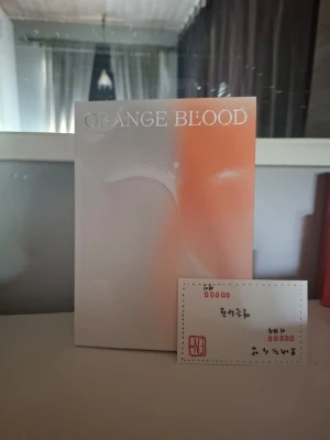 Orange Blood bok Heeseung - Säljer boken 'Orange Blood' med ett stilrent omslag i vitt och orange. Boken har tryckt text i orange och vitt och kommer med tillhörande kort och illustration. Perfekt för dig som gillar modern skönlitteratur och snygg design.