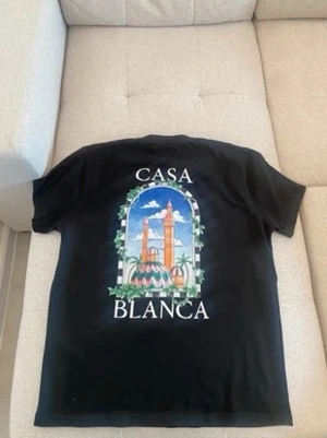 Svart Casa Blanca t-shirt med tryck - Snygg svart t-shirt med stort färgglatt tryck på ryggen som föreställer ett fönster med palmer och byggnader samt texten 'Casa Blanca'. T-shirten har rund hals och korta ärmar, perfekt för en avslappnad stil.