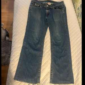 Blåa True Religion jeans - Säljer ett par blå jeans från True Religion. Jag är osäker på vilken storlek det är men mått finns på bilderna. På loggan där bak står det row 38 och seat 33. De är lite trasiga nertill på bakre sida. Skriv om ni har frågor!  