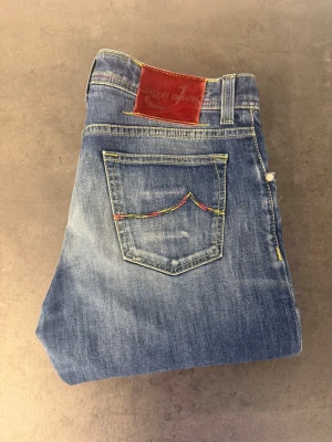 Jacob Cohën 622 Comfort jeans, stl 32 - Säljer ett par klassiska blå jeans med raka ben och snygga slitningar på låren. Jeansen har kontrastsömmar på bakfickan och en läderpatch i midjan. Tillverkade i denim med en cool vintagekänsla. Perfekta till vardagslooken!
