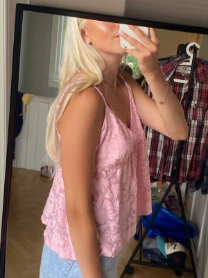 Rosa linne - Supersöt ljusrosa linnetopp med blommigt mönster och v-ringad hals. Toppen är ärmlös och har en lös passform, perfekt till jeans eller kjol. Materialet känns lätt och luftigt, vilket gör den skön att bära under varma dagar.