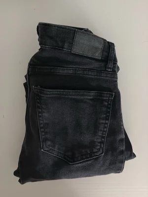 Svarta bootcut jeans - Snygga svarta jeans med bootcut-modell och klassiska bakfickor. Jeansen har en hög midja och är tillverkade i ett mjukt denimtyg med lite stretch för extra komfort. Perfekta för dig som gillar en tidlös och clean look.