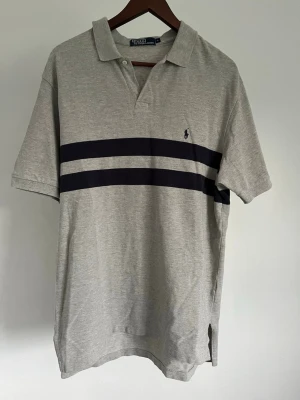 Polo by Ralph Lauren pikétröja - Polo by Ralph Lauren pikétröja Storlek: L Passform: Regular Fit Krage: Klassisk Pikékrage Material: Bomull Mått: Bröstvidd 116 cm, längd 80 cm, axel 52 cm Skick: Denna pikétröja är i ett väldigt fint skick utan defekter  Nypris cirka: 900 kr