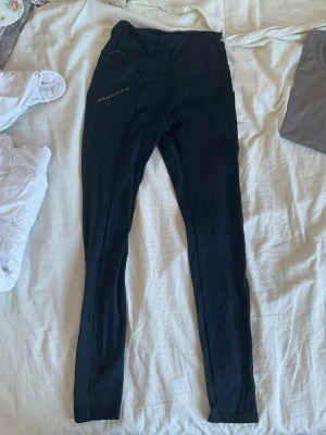 Svarta leggings från Röhnisch - Snygga svarta leggings från Röhnisch med diskret logga på vänster lår. De har hög midja och smal passform som sitter tight längs benen. Perfekta för en sportig och avslappnad stil. Materialet ser stretchigt och bekvämt ut. Det finns en ficka på höger sida. Jättesköna!