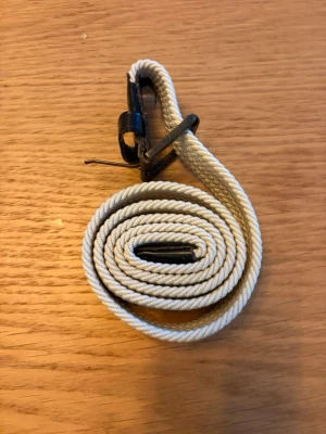 Beige flätat bälte med metallspänne - Snyggt beige flätat bälte med metallspänne och detaljer i svart. Perfekt för att ge din outfit en clean och stilren touch. Bältet är gjort i ett tåligt material och passar till både jeans och byxor.