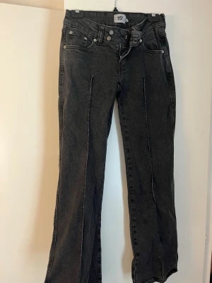 Svarta raka jeans med pressveck - Snygga svarta jeans med bootcut och markerade pressveck framtill. Jeansen har fem fickor, låg midja och dubbla knappar i linningen. Materialet är klassisk denim i bomull med en lätt tvättad look. Perfekta för en trendig stil. Innerbensmåttet är 78 cm.