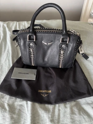 Zadig&Voltaire sunny bag - Zadig&Voltaire sunny bag. Liten modell. Köpte för 5000 kr förra året. Väskan är i superfint skick utöver att den fått lite missfärgning på nitarna i bild 6 men ingenting som alls är synligt i första hand! Ljuset på bilderna kan göra att man uppfattar även märket som missfärgat men så är inte fallet💞 Inhandlad på Zalando och är helt äkta. Dustbag och äkthetsbevis med serienummer tillkommer som ni ser i bilderna! 💞 Hoppas min fina väska får en ny ägare
