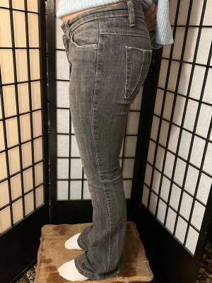 Lee Bootcut Jeans Grå Y2K W29 XS/S - Mörkgrå Lee bootcut-jeans med klassisk Y2K-passform. Låg/normal midja, lätt stretch och snyggt utsvängda ben. Mörk tvätt som passar till allt och rå fåll nedtill för en avslappnad vintagekänsla. Fint använt skick.  📏 Midja 37 cm (platt) • Innerben 78 cm • Ytterben 90 cm • Front rise 20 cm • Lår 21 cm • Benöppning 21 cm.  Passar ca W29 / XS–S – se måtten. 👖✨