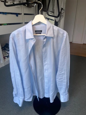 Ljusblå linneskjorta - Stilren linneskjorta från Massimo Dutti i en elegant ljusblå nyans. Skjortan har en klassisk krage, knappstängning framtill och en avslappnad passform som ger en tidlös och sofistikerad look. Tillverkad i ett svalt och luftigt linnematerial som gör den perfekt för både varma sommardagar och mer uppklädda tillfällen. Enkel att matcha med både chinos, jeans eller shorts för en stilren outfit. Ett kvalitetsplagg med hög komfort och en klassisk design som aldrig går ur tiden.