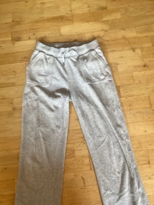 Grå mjukisbyxor från Juicy Couture - Säljer ett par grå mjukisbyxor från Juicy Couture i storlek S dom sitter lite som M, med bred resår i midjan och snörning. Byxorna har raka ben och två stora fickor fram. Materialet är en mjuk blandning av bomull och polyester, perfekta för chill dagar.