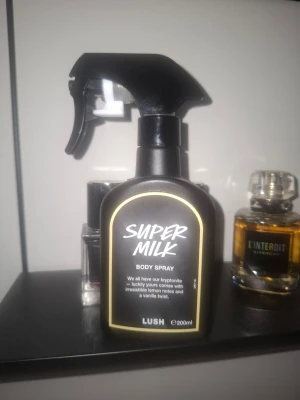 Super Milk Body Spray från Lush - Super Milk Body Spray från Lush i en svart sprayflaska med vit text och guldkant. Doften har inslag av citron och vanilj. Flaskan rymmer 200 ml och har en praktisk sprayfunktion för enkel applicering. Endast testsprayad. 