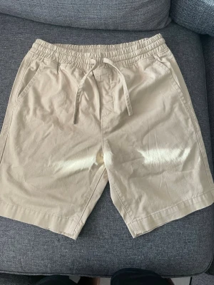 Beige shorts från Race Marine - Säljer ett par snygga beige shorts från Race Marine med elastisk midja och snörning. De har två sidofickor och är tillverkade i mjuk bomull, perfekta för varma dagar. Enkel och clean design som passar till det mesta.