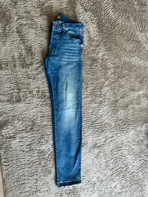 Slim fit jeans från Jack & Jones - Säljer ett par blå slim fit jeans från Jack & Jones, modell Skinny Glenn. Jeansen har klassisk femficksdesign, normalhög midja och snygga slitningar framtill. Perfekta för dig som gillar en smalare passform och tidlös denimstil.