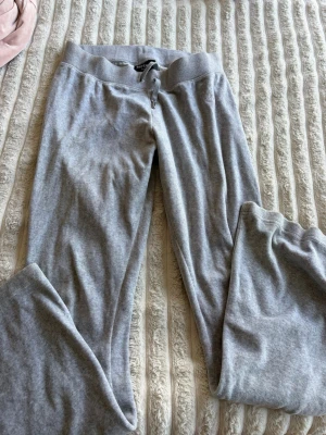 Grå mjukisbyxor juice couture - Säljer ett par klassiska grå mjukisbyxor med bred resår i midjan och dragsko. Byxorna har raka ben och är gjorda i ett mjukt och skönt material, perfekta för chill dagar hemma eller när du vill vara bekväm.