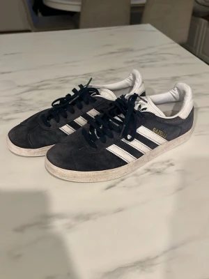 Adidas Gazelle mörkblå sneakers - Snygga Adidas Gazelle sneakers i mörkblå mocka med vita detaljer och klassiska tre ränder på sidan. Lite smutsig skosula enligt bild.