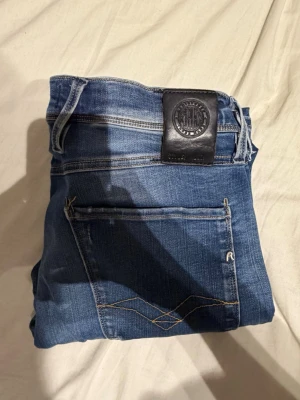 Replay anbass jeans  - Snygga blå jeans med klassisk femficksdesign och kontrastsömmar på bakfickan. Jeansen har en svart patch i midjan och är tillverkade i denim med en lätt tvättad look. Perfekta för en avslappnad och trendig stil.