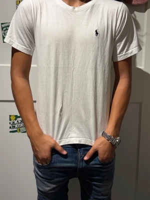 Vit Ralph Lauren T-shirt  - Klassisk vit t-shirt med korta ärmar och v-ringad hals. Liten broderad logga på bröstet. Enkel och stilren design som passar till det mesta. Tillverkad i mjukt bomullsmaterial för en skön känsla.