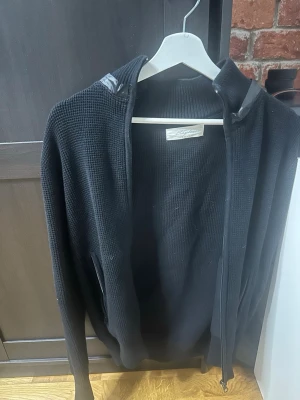 Svart ziptröja med avtagbar huva från sayless  - Säljer en svart ziptröja med huva i ribbstickat material. Tröjan har dragkedja framtill, långa ärmar och fickor på sidorna. Perfekt för en avslappnad och stilren look. 