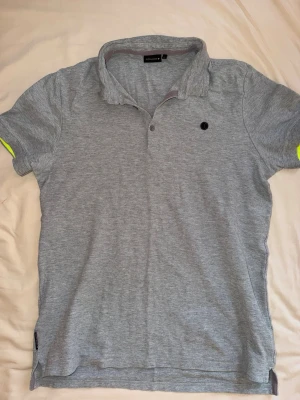 Björn Borg piké T-shirt  - Grå piké T-shirt med neongula detaljer från Björn Borg i storlek L. Perfekt till träning, så som tennis, men även till vardags. Toppenskick!