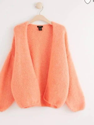 Ljusorange fluffig kofta , helt ny, nypris 400 - Supermjuk och fluffig ljusorange kofta med öppen front och avslappnad passform. Koftan har långa ärmar och är stickad i ett lurvigt material som ger en mysig känsla. Perfekt för lager på lager och en färgklick i garderoben.