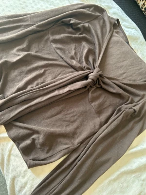 Brun knyt topp v-ringning - Ber om ursäkt för så dålig kvalite på bilderna men det är brun färg på tröjan och ändå ganska så nytt skick. Trendig brun omlottopp med lång ärm och knyt framtill som ger en öppen look. Toppen har v-ringad hals och är tillverkad i mjukt material, perfekt för att styla med kjol eller jeans. Ärmarna är långa och lätt utsvängda för en cool vibe.