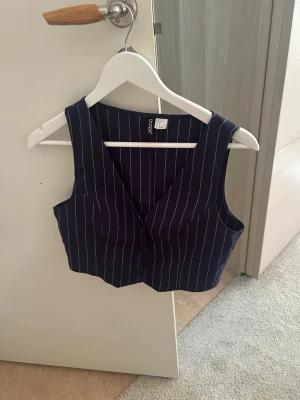 Mörkblå randig väst med knappar - Snygg mörkblå väst med vita ränder och knäppning framtill. Västen har en croppad passform och djup v-ringning, perfekt att styla över en t-shirt eller skjorta för en trendig look. Sitter tajt till kroppen också💙🐠