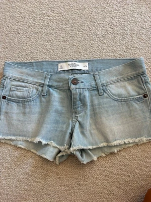 Ljusblå jeansshorts Abercrombie - Säljer ett par ljusblå jeansshorts från Abercrombie & Fitch. De har råa, fransiga kanter, klassisk femficksdesign och bälteshällor. Perfekta för varma dagar och har en avslappnad vibe.💓