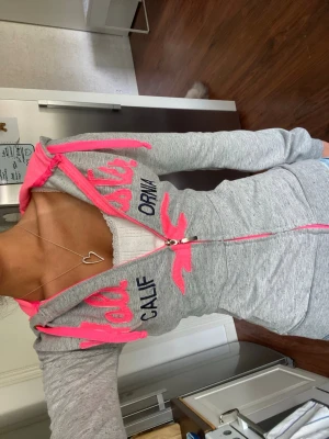 Ljusgrå tajt Hollister zip hoodie med rosa broderi - Gullig Hollister zip hoodie med neon ish rosa broderi över bröstet och hollister logan, strl M (omsydd till xxs) följ för fler liknande abercrombie/ hollister hoodies!