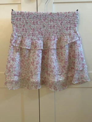 Blommig volangkjol i pastellfärger från Gina Tricot - Söt kortkjol med blommigt mönster i rosa och grönt på vit botten i storleken 146/152. Kjolen har smock i midjan och dubbla volanger för en luftig och fin look. Perfekt för vår och sommar, till både sneakers och sandaler. Har använt några gånger 💕 40 kr + frakt